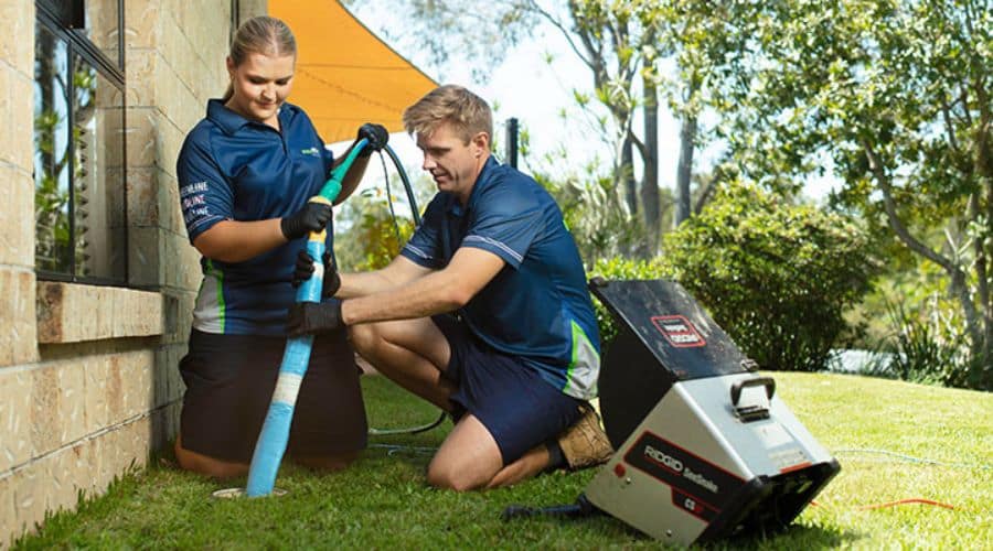 Female and male plumbers using trenchless plumbing technique to repair pipes