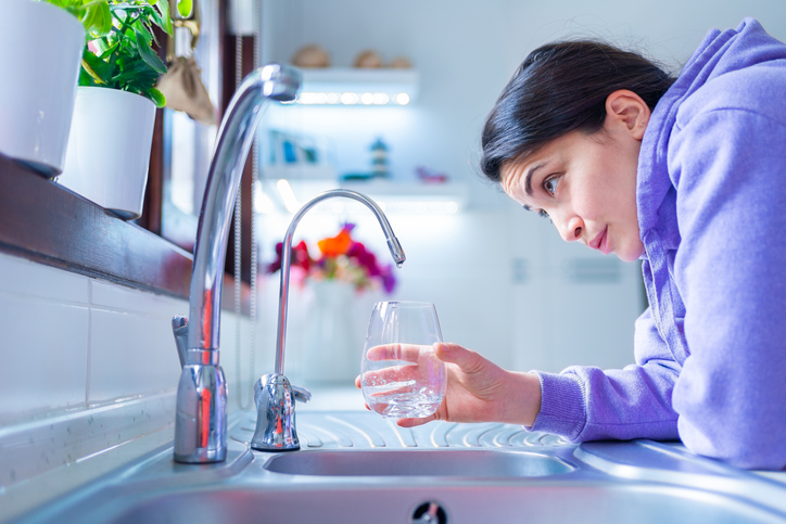 Woman trying to poor a glass of water from a faulty kitchen sink only getting drips